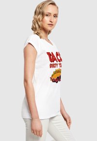 Hvid bomulds T-shirt med fed rød tekst, der står "TACO DIRTY TO ME," samt en farverig taco-grafik, afslappet pasform og korte ærmer.