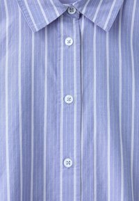 Chemise bleu clair avec de fines rayures verticales blanches, dotée d'un col pointu et de quatre boutons blancs sur le devant.