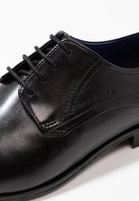 Chaussure habillée en cuir noir à finition lisse, design à lacets, avec un logo embossé discret. Présente une forme classique et une semelle durable.