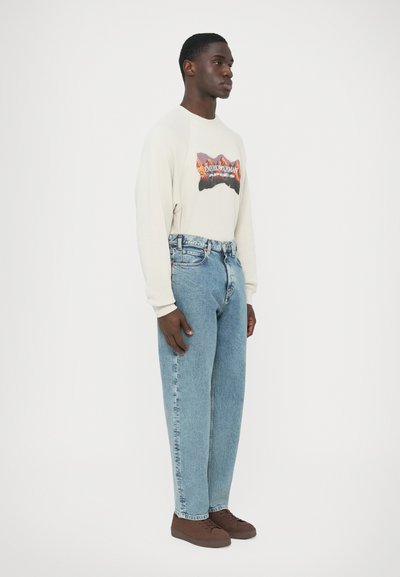 Ανοιχτό μπεζ φούτερ με γραφικό βουνό, σε συνδυασμό με ανοιχτό μπλε τζιν παντελόνι. Καφέ παπούτσια ολοκληρώνουν το ντύσιμο.