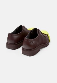 Scarpe in pelle marrone con una finitura testurizzata, caratterizzate da un accento in gomma gialla nella parte anteriore e una suola in gomma marrone resistente.