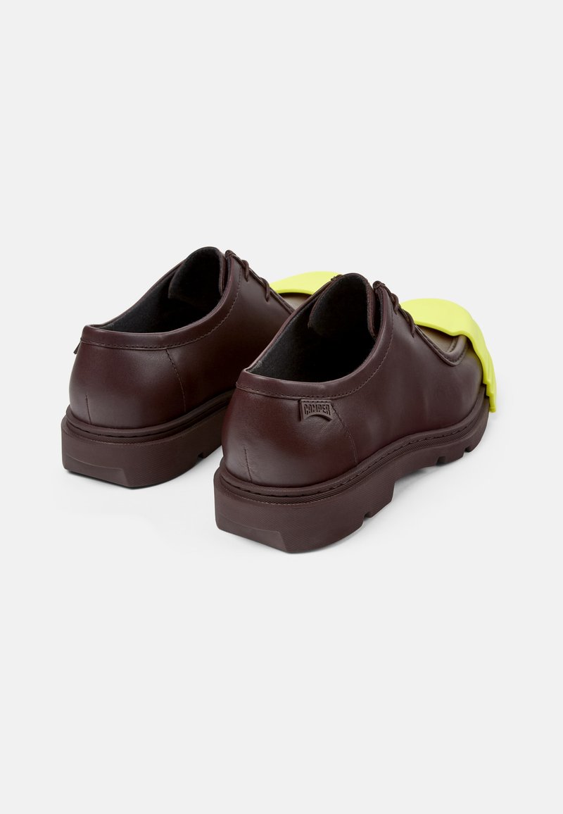 Brązowe skórzane buty o teksturowanym wykończeniu, z żółtym akcentem z gumy z przodu oraz trwałą brązową gumową podeszwą.