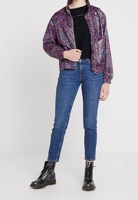 Veste bomber colorée et à motifs avec fermeture éclair à l'avant, assortie à un t-shirt noir et à un jean skinny bleu. Des bottes de combat noires à lacets complètent le look.