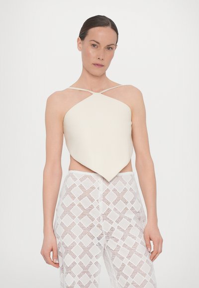 Crème-kleurig, matte satijnen top met een diamantvorm en kruislings straps, gecombineerd met doorschijnende witte broeken met een diamantpatroon.