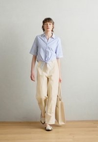 Stripete blå og hvite skjorter med knyting i livet, kremfargede bukser med vidde og en beige tote bag. Brukt med svarte og hvite leiligheter.