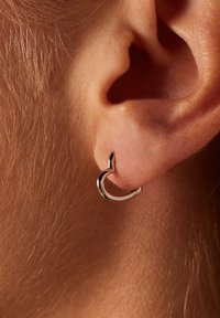 Silberne Creolen mit einem geschwungenen Design, das eine polierte Oberfläche und einen kleinen spitzen Akzent zeigt, die am Ohrläppchen befestigt sind.