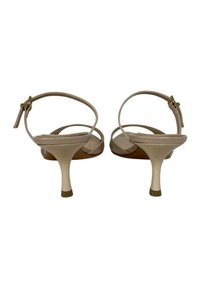 Sandali beige con tacco, dotati di sottili cinturini alla caviglia, schienale aperto e suole testurizzate. Presentano un tacco sottile con un accento dorato alla base.