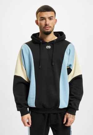 Čierna mikina s modrými a krémovými farebnými blokmi, s viazacou šnúrkou, nášivkou a rebrovaným lemom. Vyrobená z mäkkej látky.