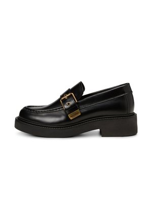 Mocassino in pelle nera con una spessa suola a cuneo nera, caratterizzato da una fibbia in ottone e cuciture decorative lungo il bordo superiore.