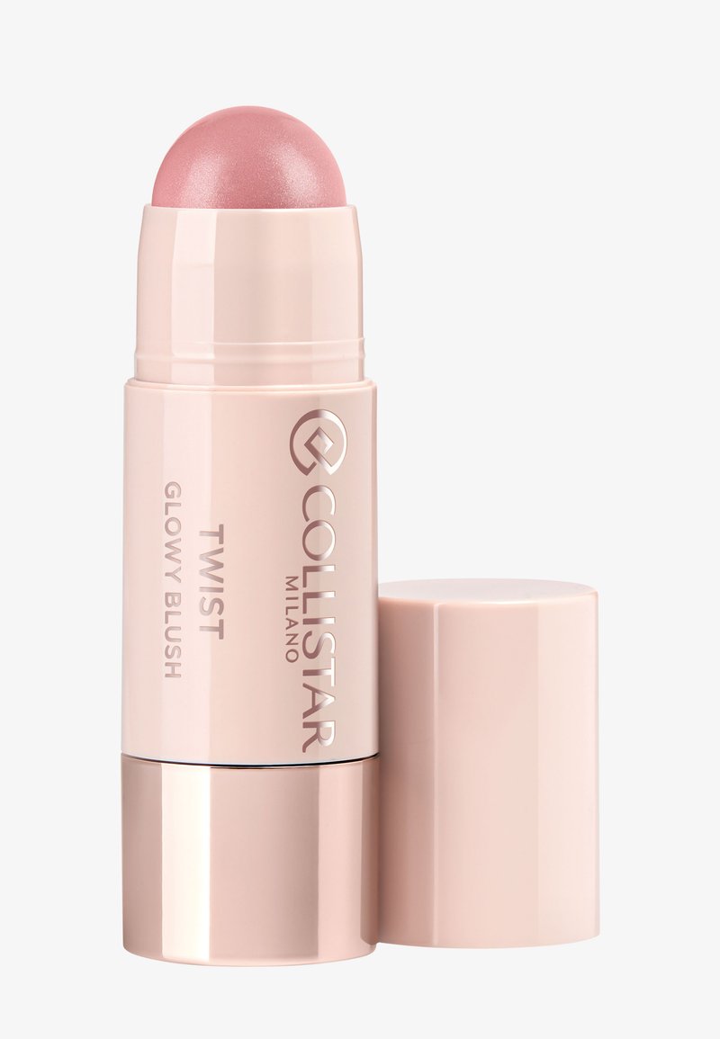 Bâton de blush rétractable avec un capuchon métallique rose arrondi, texture crémeuse et fini brillant. Présente un emballage élégant rose pâle avec le logo de la marque.
