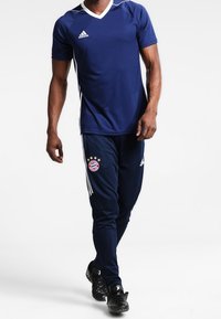 Mörkblå Adidas sportkläder med en kortärmad tröja med vita detaljer och matchande byxor med Bayern Münchens logotyp och tre ränder.