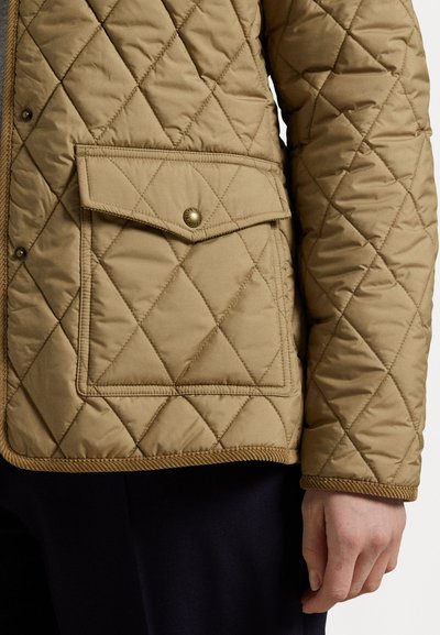 Gequiltede tan jas met een voorzak met een drukknoopsluiting, contrasterende stikdetails en een gladde textuurafwerking.