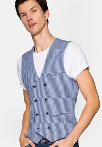 Niebieska i biała kamizelka w kratkę z podwójnym zapięciem na guziki, klapami typu notch oraz jedną kieszenią na piersi, połączona z białym T-shirtem.