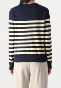 Granatowo-kremowy sweter w paski z dzianiny z okrągłym dekoltem, wyposażony w prążkowany dół i mankiety, prezentowany na plecach modela.