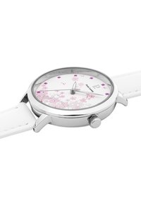 Reloj blanco con caja de acero inoxidable, patrón floral en tonos rosa y púrpura en la esfera, y correa de cuero blanco suave. Incluye una corona para ajustar la hora.