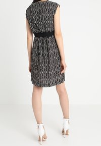 Černé šaty s kruhovým vzorem, s krátkými rukávy a přiléhavým pasem. V kombinaci s bílými vysokými podpatky, které mají elegantní design.