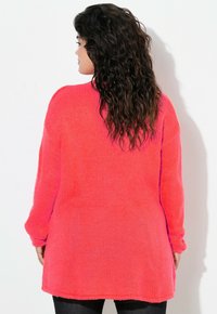 Rosa gestrickter Pullover mit lockerer Passform, langen Ärmeln und geripptem Muster, der hinten länger ist als vorne.