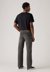 Black short-sleeve t-shirt, gray straight-leg jeans with a leather patch on the back, and black sneakers. Simple design and solid colors.