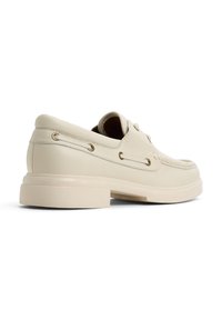 Beige lädersko för båt med rund tå, platt gummisula och dekorativ snörning med metallöglor på sidorna.