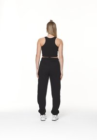 Svart ribbet croptop kombinert med svarte, løse joggebukser og hvite sneakers, sett fra baksiden mot en enkel hvit bakgrunn.