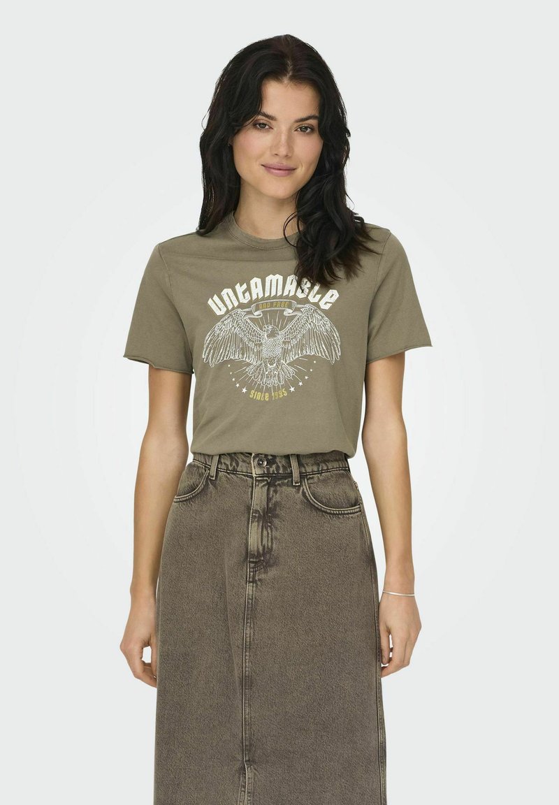 T-shirt en coton vert olive avec un graphique d'aigle blanc et le texte "INDOMPTABLE", associé à une jupe en denim délavée taille haute.