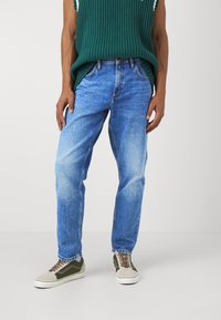 Jeans din denim de o nuanță albastru deschis, cu un croi lejer, având cusături proeminente și un finisaj ușor decolorat. Asortează-te cu adidași verzi și bej.