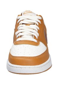 Sneaker Nike Court Vision avec une tige en cuir beige, une boîte à orteils perforée blanche, des lacets blancs et une semelle en caoutchouc texturée avec des accents mouchetés.