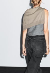 Top in cotone grigio a maglia con scialle marrone chiaro appoggiato su una spalla, abbinato a jeans neri a vita alta. Design casual e semplice.