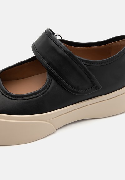 Sort lædersko med en bred strop og velcro-lukning, der har en cremefarvet platformssål og rund tådesign. Glat tekstur hele vejen igennem.