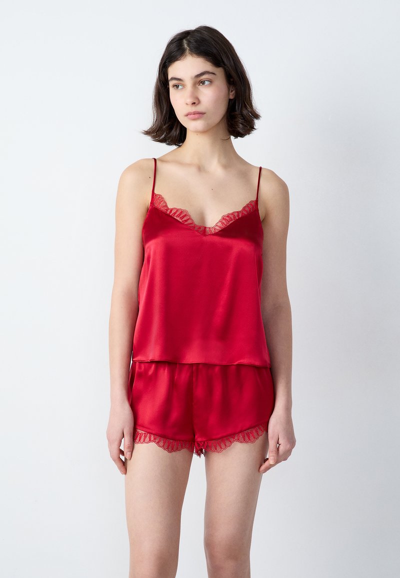 Set di pigiama in satin rosso composto da un top con pizzo e pantaloni corti coordinati con bordi in pizzo. Tessuto morbido e liscio, vestibilità rilassata.