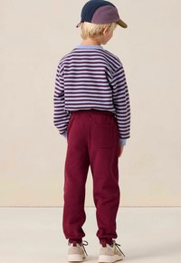 Gestreiftes Langarmhemd in Blau und Burgunderrot, kombiniert mit burgunderroten Jogginghosen mit einer Gesäßtasche. Weicher Stoff, lässige Passform.