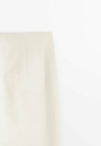 Gros plan d'une jupe blanche avec une taille haute et une poche plaquée unique sur le côté, réalisée en tissu texturé.