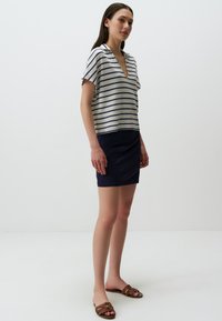 Top a righe a maniche corte in beige e blu scuro, con scollo a V e vestibilità comoda, abbinato a una mini gonna in denim scuro e sandali piatti marroni.