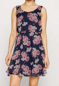 Marinblå blommig klänning med rundad halsringning, ärmlös design och elastisk midja. Har mönster med rosa rosor och en svängd fåll.