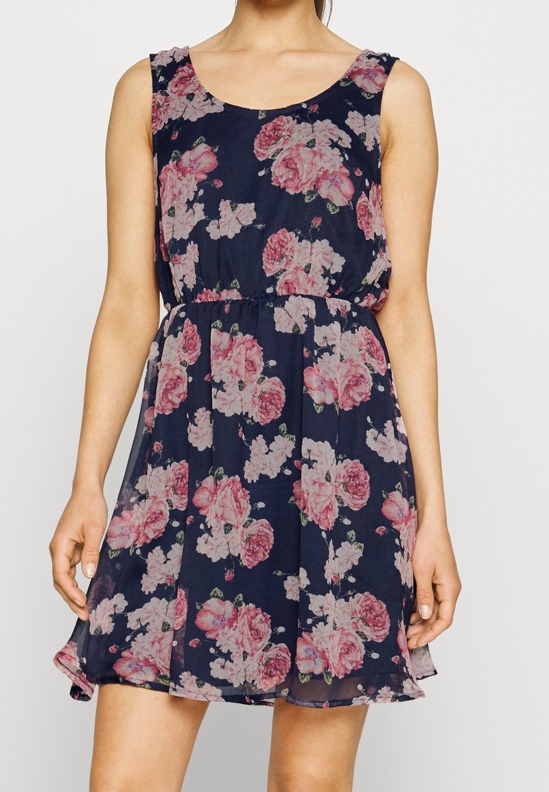 Marinblå blommig klänning med rundad halsringning, ärmlös design och elastisk midja. Har mönster med rosa rosor och en svängd fåll.