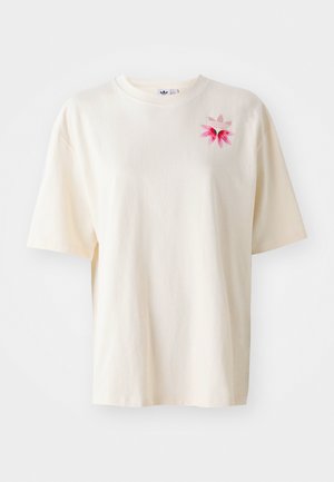 Lys beige bomulls t-skjorte med en rosa blomst og logo broderi på venstre bryst. Løs passform, korte ermer, rund hals.