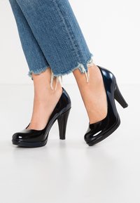 Décolleté in vernice nera con tacco alto e punta arrotondata, abbinati a jeans in denim con orlo sfilacciato.