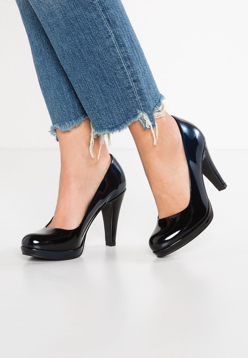 Décolleté in vernice nera con tacco alto e punta arrotondata, abbinati a jeans in denim con orlo sfilacciato.