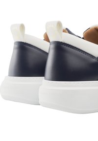 Baskets en cuir bleu marine avec des accents blancs, présentant un design minimaliste, une forme arrondie et une semelle blanche texturée. Marque sur le tirant arrière.