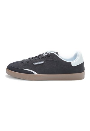 Sneaker in suede nero con accento bianco sul tallone e suola in gomma marrone. Presenta lacci grigi e dettagli cuciti sulla tomaia.