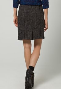Falda de tweed gris con una ligera forma en línea A, con detalles de costuras frontales y un pliegue en la parte trasera, combinada con botas negras hasta el tobillo.