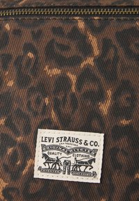 Levi Strauss & Co. szövetcímke barna és fekete leopárdmintás farmeren, látható cipzárvarrással.