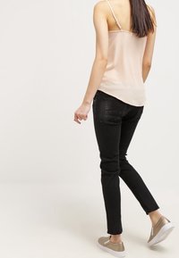 Světle růžová saténová dámská košilka s tenkými ramínky, spárovaná s černými slim-fit džíny a béžovými teniskami s metalickými akcenty.