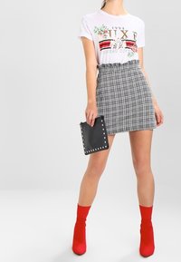 T-shirt graphique blanc avec un motif floral, associé à une jupe à carreaux grise. Une pochette noire et des bottines rouges viennent compléter la tenue.