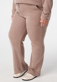 Wafeltextuur, lichtbruine broek met een relaxte fit en zakken, gecombineerd met ivoorkleurige schoenen met gouden studs.