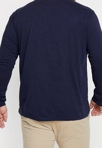 Navyblaues Langarm-T-Shirt aus weichem Baumwollstoff mit abgerundetem Saum und schlichtem Design, von hinten präsentiert, ohne grafische Details.