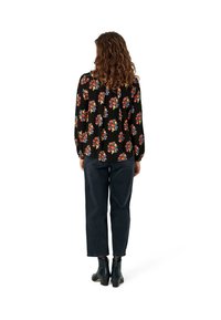 Black blouse with colorful floral pattern, long sleeves, relaxed fit, paired with dark denim pants and black heeled ankle boots.