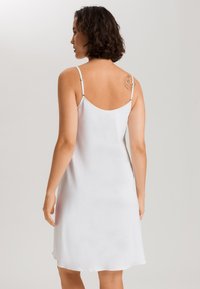 Abito da notte bianco e leggero con spalline sottili, texture liscia e design fluttuante. Presenta un orlo arrotondato e uno stile minimalista.