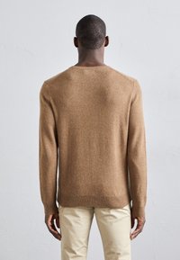 Pull en laine marron avec un col rond, des poignets et un ourlet côtelés, une texture lisse et une coupe décontractée, associé à un pantalon beige.