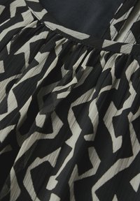 Schwarz-weißer Stoff mit zigzagförmigen Mustern, aus einem strukturierten, leichten Material und mit gerafften Details in der Nähe des Halsauschnitts.